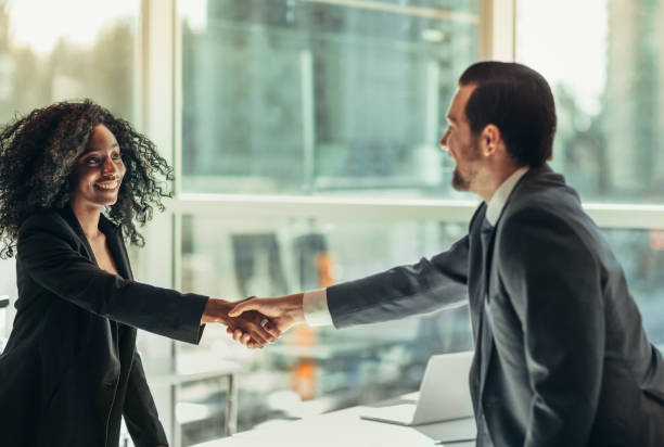 mujer de negocios negra estrecha la mano de un hombre de negocios en el escritorio de la mesa en una oficina de negocios moderna bien vestida después del acuerdo de asociación entrevista de trabajo - opportunity handshake job business fotografías e imágenes de stock