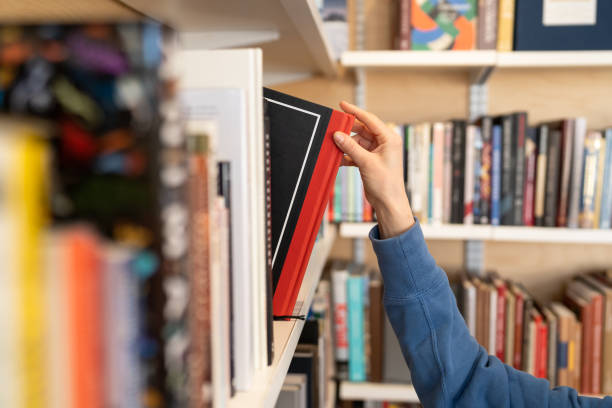 kobieta ręcznie wybiera książkę z półki w bibliotece na uniwersytecie, w college'u, liceum lub księgarni - bookstore zdjęcia i obrazy z banku zdjęć