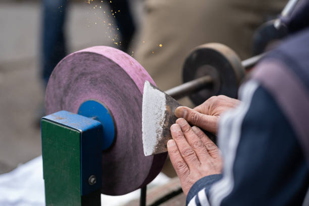 istock Master Sharpens Ax On Electric Sharpener With Bright Sparks And Holds Blade With His Brutish Fingers 1399528374