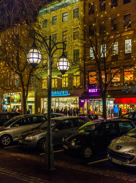 people Christmas shopping in the famous Koenigsallee illuminated by Christmas lights in Dusseldorf Germany at night. The Koenigsallee, King's Avenue, is the busiest shopping street in Germany with many upmarket luxury retail stores.