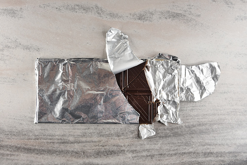 Chocolate bar pieces in the foil package on the table, cracked chocolate bar