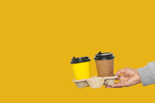 Collage with a hand holding two cups of coffee on a yellow background. There is space for text.