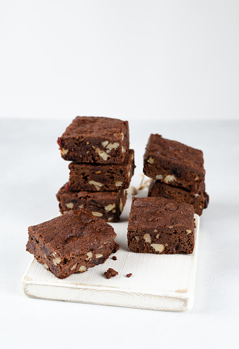 Chocolate homemade brownies with dried cranberries and walnuts on the white wooden board with white background