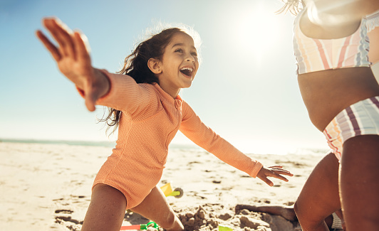 Fun-loving little girl playing with her friends at the beach. Adorable young girl laughing happily with her arms outstretched. Carefree kids enjoying themselves during summer vacation.