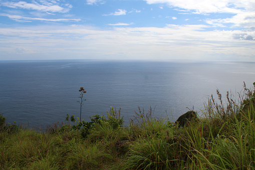 Ocean view from the edge of the green hill with bright blue sky over horizon at day time. Nusa Panida, Bali, Indonesia