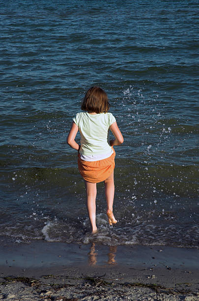 Little girl on beach Little girl in orange  skirt on beach splashing the water with her feet. alintal stock pictures, royalty-free photos & images