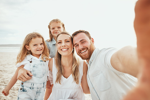 Cheerful caucasian family taking selfie together on beach. Handsome man looking happy while taking picture with his wife and two daughters while on vacation