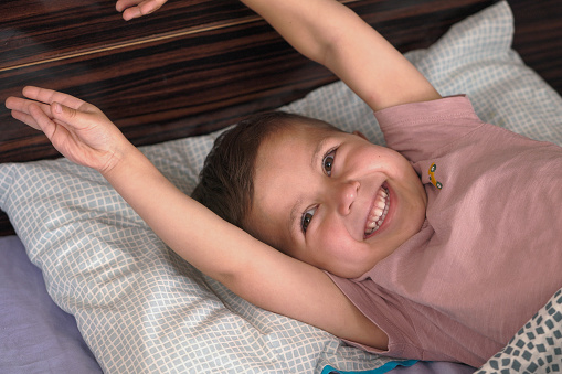 Adorable child wake up and stretch with smile on his bed in a room.