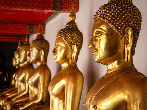 Gallery of Golden Buddhas in the bhumisparsha position in a temple in Bangkok, Thailand. Gallery with golden Buddha images. Buddha image covered with gold