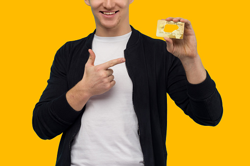 Handsome sporty guy pointing finger gold credit card on a yellow background.