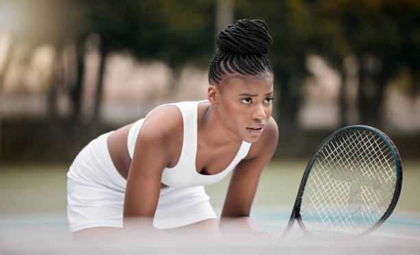 skupiona kobieta czekająca podczas meczu tenisowego. młoda afroamerykanka trzymająca rakietę podczas gry w tenisa. zawodowy sportowiec stojący na korcie tenisowym. młoda kobieta grająca w tenisa - action tennis women tennis racket zdjęcia i obrazy z banku zdjęć