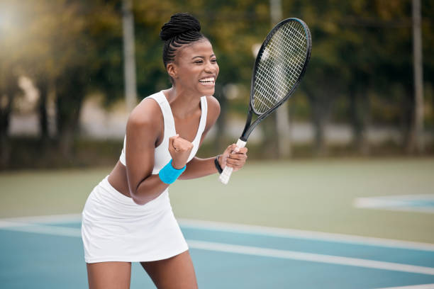 excited tennis player cheering during a match. cheerful tennis player celebrating her success after a game. young african american athlete playing a game of tennis. girl playing tennis - womens tennis imagens e fotografias de stock