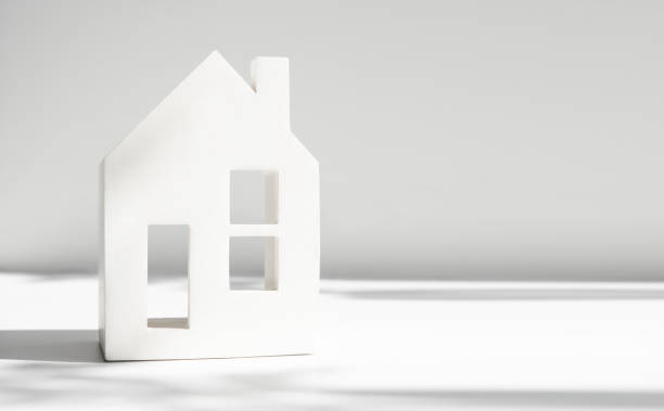 istock Banner with a white ceramic house standing on a light gray background with a beautiful shadow from the plant. The concept of housing, mortgage, background with copy space. 1399548081