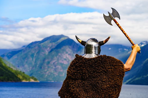 Viking warrior with helmet and axe on fjord shore in Norway. Tourism and traveling concept