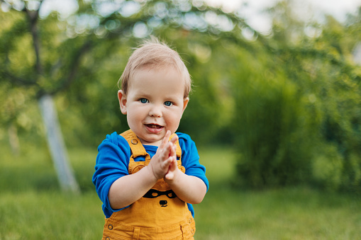 Smiling kid claps his hands in the park or garden of a summer park. Blurred background, place for text