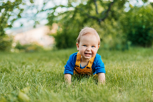 A baby boy lies on the grass in the garden and laughs.