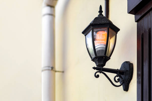 istock black iron wall lantern in retro style with glass shade and electric light bulb glow with warm light, urban wall lighting on facade of building with downspout pipe, decorative lamp close-up, nobody. 1399553843