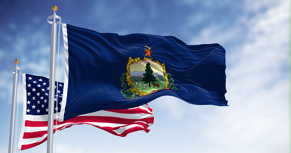 The Vermont state flag waving along with the national flag of the United States of America. Vermont is a state in the New England region of the United States