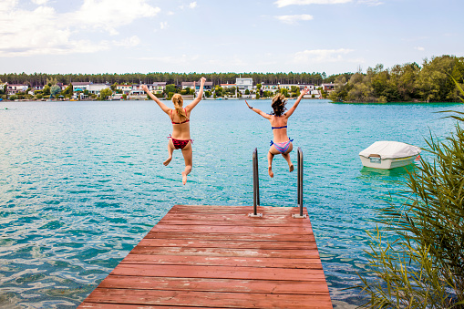 Two female friends jumping into the lake on a sunny summer day