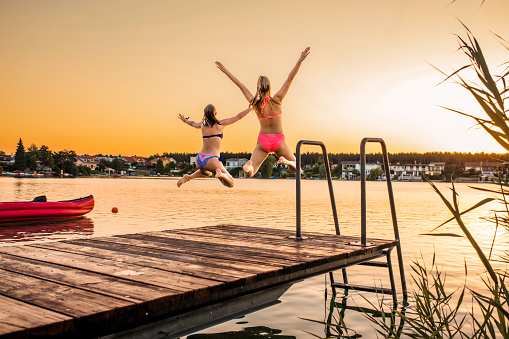 Two female friends jumping into the lake at sunset