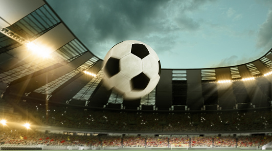 Flight of soccer football ball through crowded stadium with spotlights in evening time. Concept of sport, art, energy, power. Poster for ad, design. Creative collage. Unfocus effect