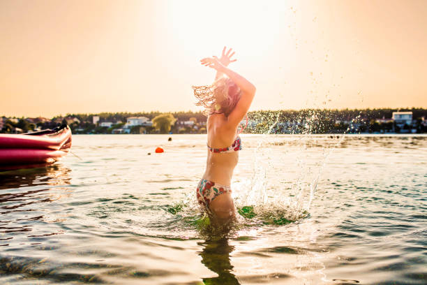 little girl in a summer swimsuit at sunset by the sea. a girl stands waist-deep in water and examines her carefully, the child is illuminated by the rays of the setting sun