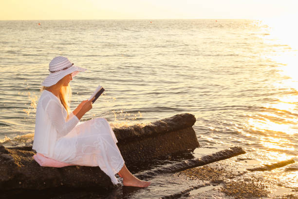 istock Young woman reading a book while relaxing on tropical beach at sunset 1399554630