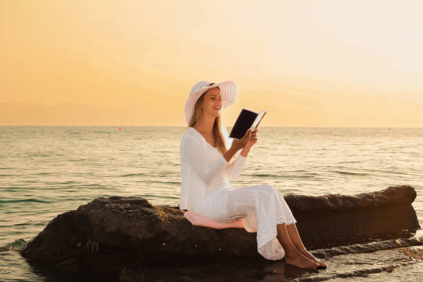 istock Young woman reading a book while relaxing on tropical beach at sunset 1399554672