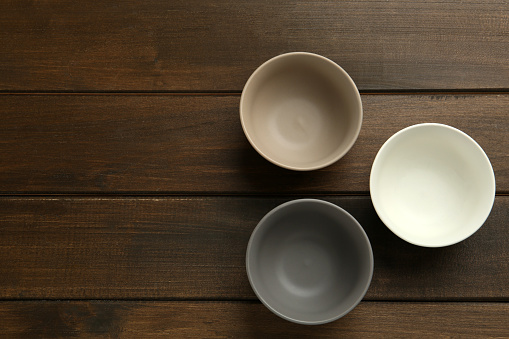 Stylish empty ceramic bowls on wooden table, flat lay and space for text. Cooking utensils