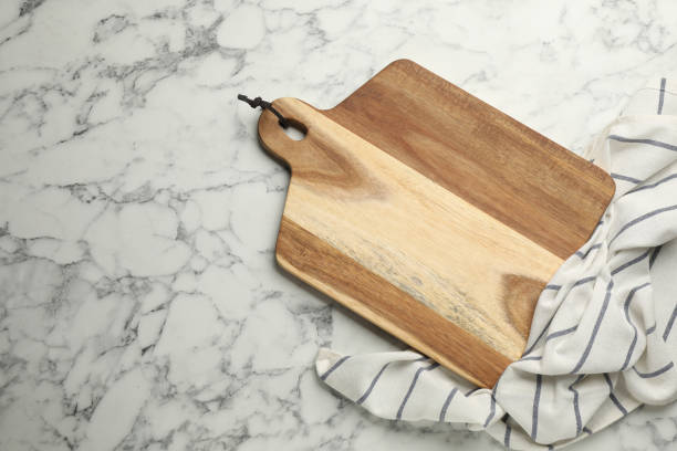 istock Wooden cutting board and kitchen towel on white marble table, flat lay with space for text. Cooking utensil 1399556275