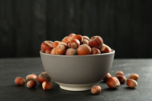 Ceramic bowl with hazelnuts on black table. Cooking utensil