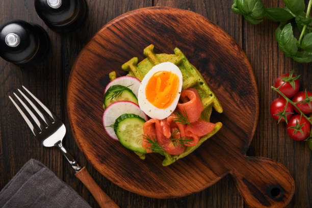 istock Savory waffles. Breakfast green waffles wild garlic or spinach with egg, tomato, salmon on wooden plate for breakfast on old dark wooden background. Light dinner, lunch or breakfast. Top view. Mock up 1399556470