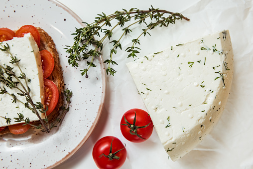 Appetizer sandwiches with cherry tomato, cheese and italian herbs on a loaf of bread, white background, flat lay