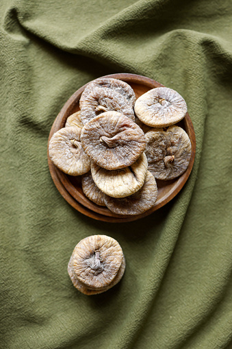 Istanbul, Turkey-May 27, 2022: Dried figs in wooden plate on khaki green linen tablecloth. Shot with Canon EOS R5.