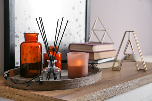 Wooden tray with air reed freshener and candles on table indoors