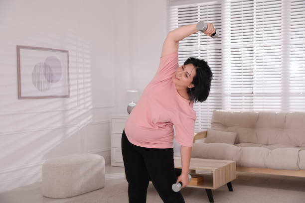 istock Overweight mature woman doing exercise with dumbbells at home 1399558848