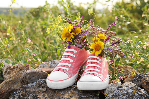 Shoes with beautiful flowers on stones outdoors