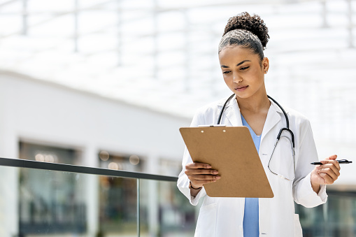 Confident serious female doctor with clipboard. Practitioner is wearing lab coat and stethoscope.