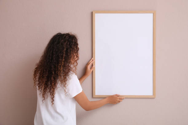 istock African American woman hanging empty frame on pale rose wall, back view. Mockup for design 1399559169