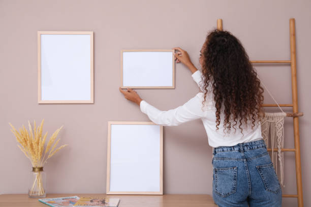 istock African American woman hanging empty frame on pale rose wall over table in room, back view. Mockup for design 1399559276