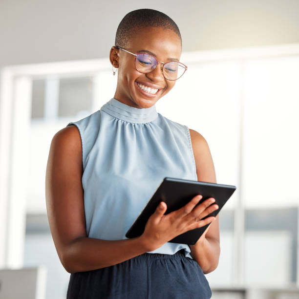 joven y alegre empresaria afroamericana trabajando sola en una tableta digital en el trabajo. mujer negra feliz sonriendo mientras usa las redes sociales en una tableta digital. empresario revisando un correo electrónico en una tableta digital - una sola mujer fotografías e imágenes de stock