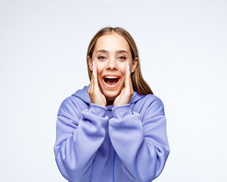 Portrait of happy teenage girl with blond hair shouting at camera against white background.