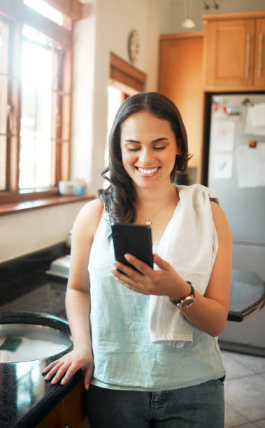 istock Happy mixed race woman smiling while using smart phone at home. Woman reading text message or chatting on social media while busy with chores in the kitchen 1399562274