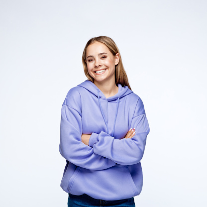 Portrait of smiling teenage girl with blond hair wearing lilac hoodie, smiling at camera against white background.
