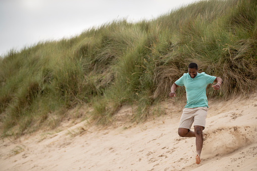 A mid adult man running down a sand bank at Beadnell beach, North East England. He is smiling and looking excited while he runs.