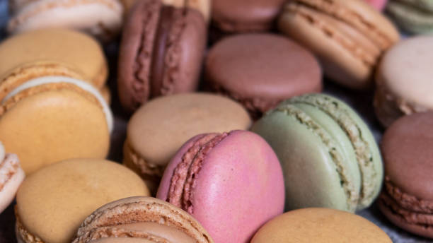 Full frame image of heap of multi coloured macarons filled with flavoured butter cream, vanilla, lemon, salted caramel, chocolate, strawberry and pistachio flavoured meringues, focus on foreground