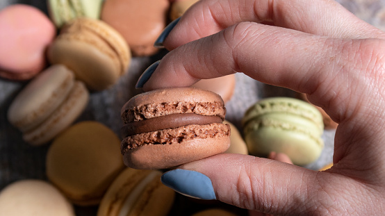Stock photo showing close-up, elevated view a pile of multi coloured macarons on wood grain background. Vanilla, lemon, salted caramel, chocolate, strawberry and pistachio flavoured macarons ready for an afternoon tea party.