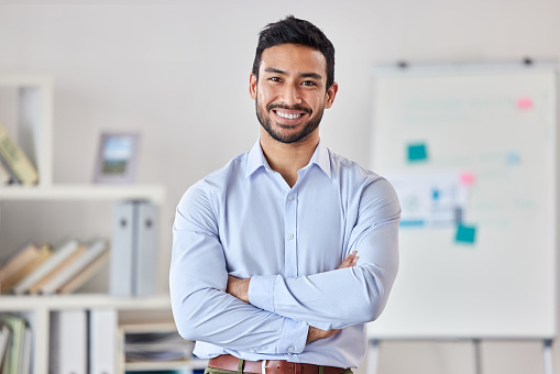 Joven empresario mestizo feliz de pie con los brazos cruzados trabajando solo en una oficina en el trabajo. Un experto orgulloso jefe hispano sonriendo mientras está de pie en una oficina photo