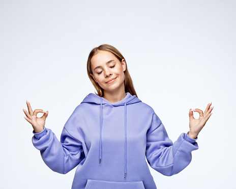 Smiling teenage girl with eyes closed gesturing peace sign against white background.
