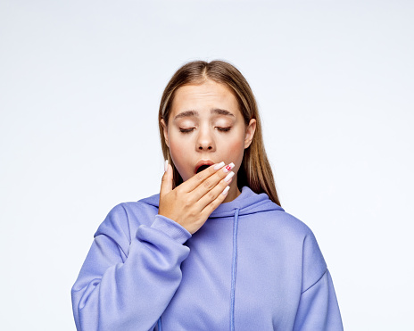 Tired teenage girl in t-shirt yawning against white background.